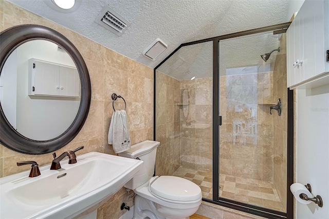 bathroom with toilet, tile walls, sink, a textured ceiling, and a shower with door