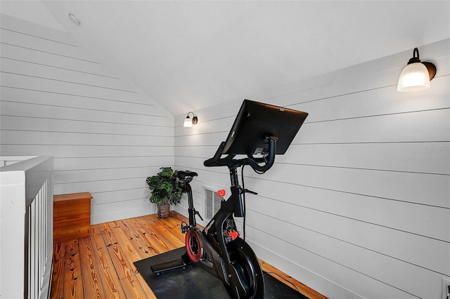 exercise area with vaulted ceiling, hardwood / wood-style floors, and wooden walls