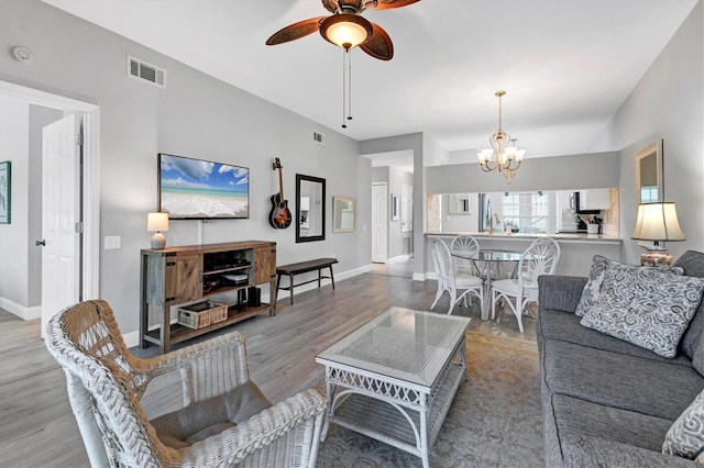 living room with ceiling fan with notable chandelier and light hardwood / wood-style flooring