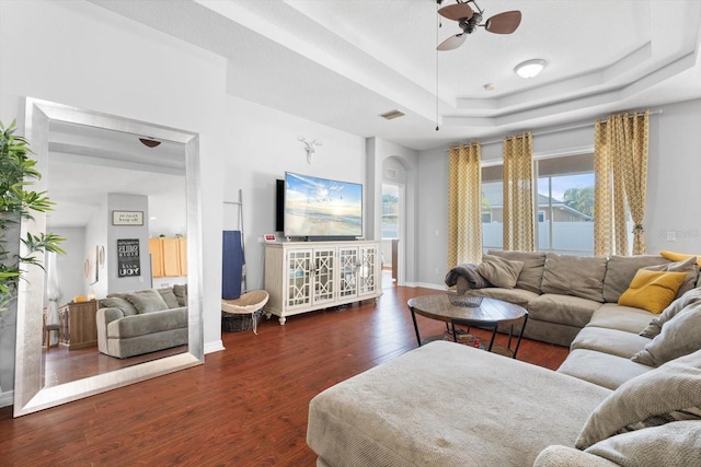 living room featuring dark hardwood / wood-style floors, ceiling fan, and a tray ceiling