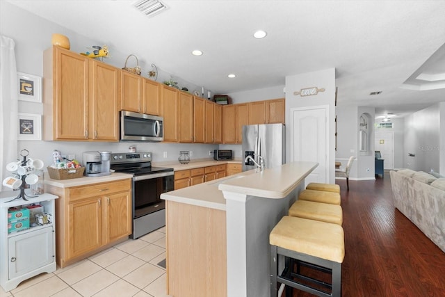 kitchen with a kitchen breakfast bar, stainless steel appliances, sink, light tile patterned floors, and an island with sink