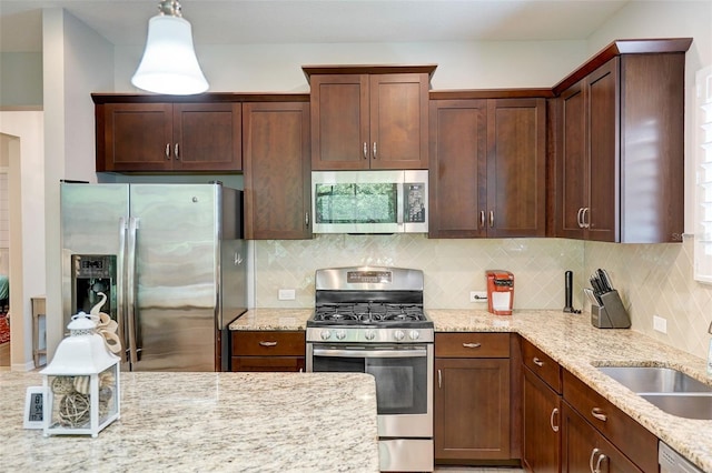 kitchen featuring decorative backsplash, light stone counters, stainless steel appliances, sink, and hanging light fixtures