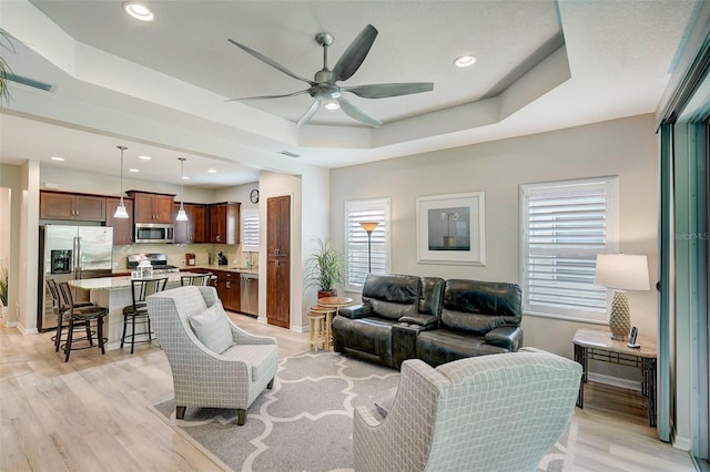 living room featuring a tray ceiling, ceiling fan, and light hardwood / wood-style flooring