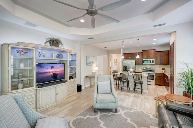 living room featuring ceiling fan, light wood-type flooring, and a tray ceiling