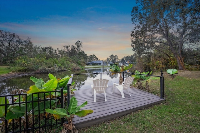 deck at dusk featuring a water view and a yard