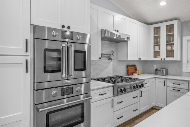 kitchen with stainless steel appliances, lofted ceiling, white cabinets, and backsplash