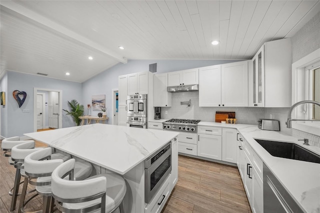 kitchen featuring stainless steel appliances, lofted ceiling with beams, white cabinets, a kitchen bar, and decorative backsplash