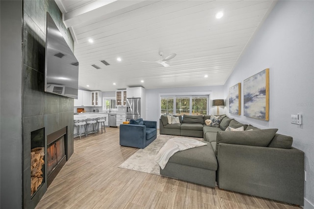 living room with a tile fireplace, vaulted ceiling, ceiling fan, wood ceiling, and light hardwood / wood-style flooring