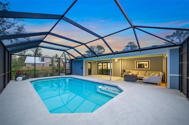 pool at dusk with an outdoor hangout area, a patio area, and glass enclosure