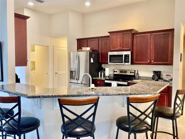 kitchen with kitchen peninsula, appliances with stainless steel finishes, light stone counters, and a kitchen breakfast bar