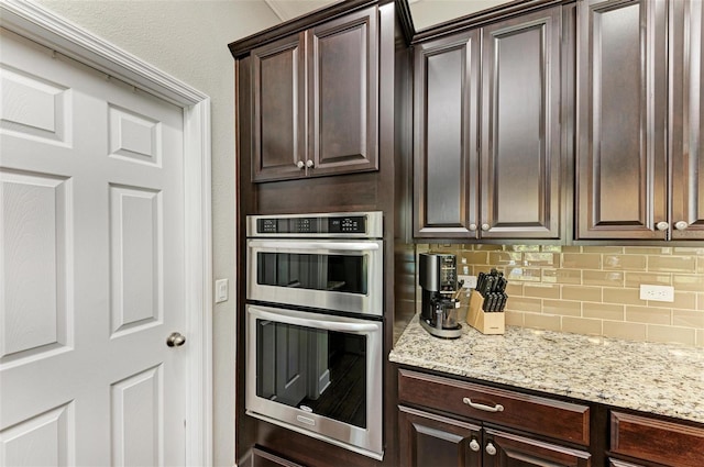 kitchen with double oven, decorative backsplash, dark brown cabinets, and light stone counters