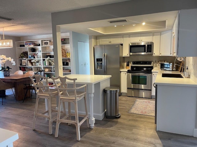 kitchen featuring appliances with stainless steel finishes, backsplash, a textured ceiling, hardwood / wood-style flooring, and white cabinets