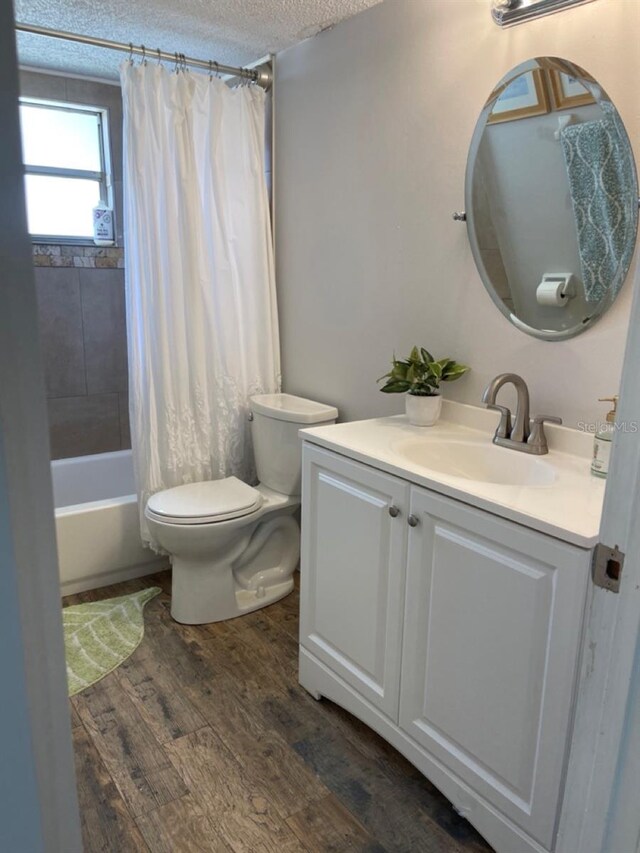 full bathroom featuring vanity, a textured ceiling, shower / bath combo with shower curtain, wood-type flooring, and toilet