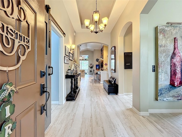 foyer entrance featuring arched walkways, a chandelier, baseboards, light wood-style floors, and a raised ceiling