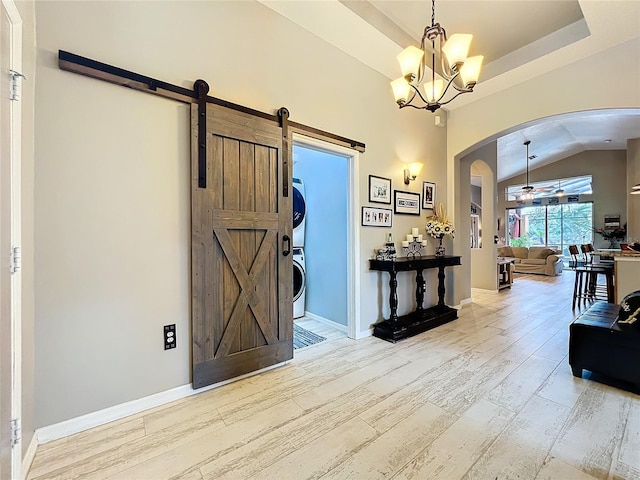 entryway featuring a barn door, arched walkways, wood finished floors, a tray ceiling, and stacked washing maching and dryer