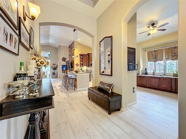 hallway with vaulted ceiling, light wood-type flooring, and arched walkways