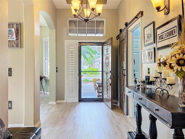 entryway featuring arched walkways, light wood finished floors, a barn door, a chandelier, and baseboards