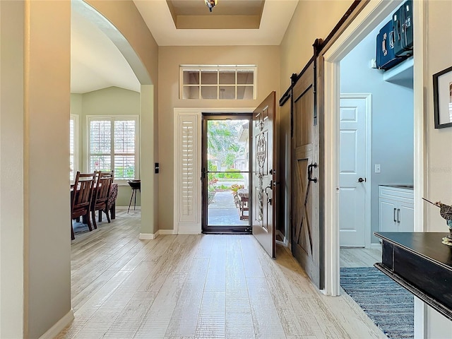 entrance foyer with arched walkways, a raised ceiling, light wood-style flooring, a barn door, and baseboards