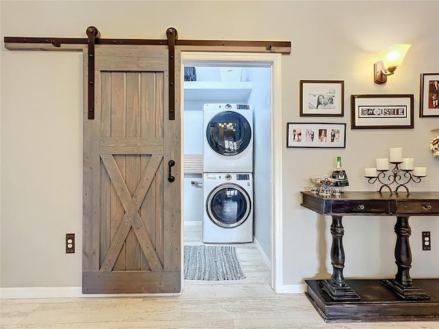 washroom featuring a barn door, laundry area, stacked washer and dryer, wood finished floors, and baseboards