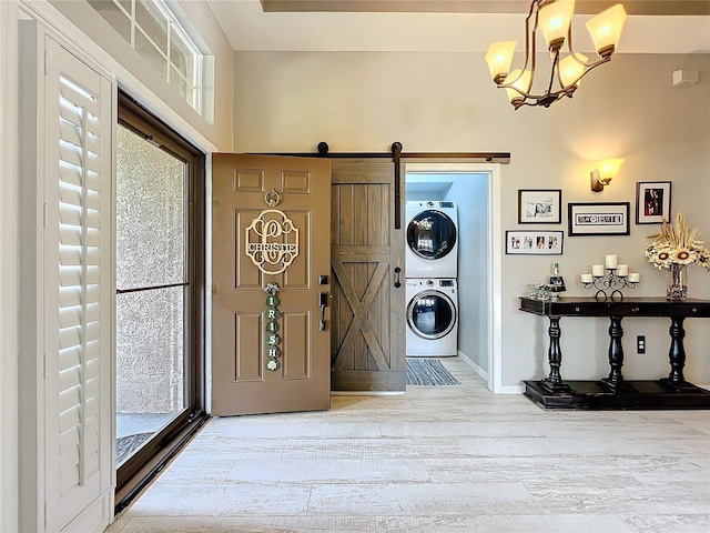 entrance foyer with light wood finished floors, a barn door, baseboards, stacked washer / drying machine, and a notable chandelier