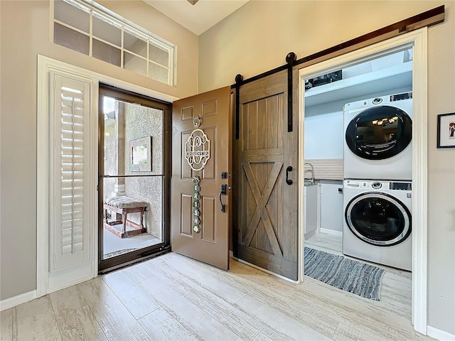 clothes washing area featuring stacked washer / dryer, laundry area, wood finished floors, and a barn door