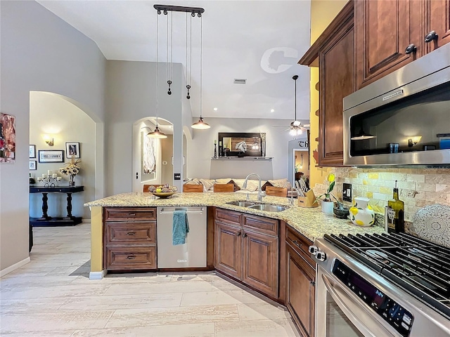 kitchen featuring stainless steel appliances, tasteful backsplash, a sink, light stone countertops, and a peninsula