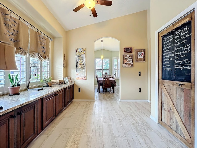 interior space with lofted ceiling, arched walkways, a healthy amount of sunlight, and light wood-style flooring