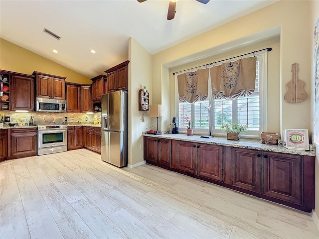 kitchen featuring visible vents, lofted ceiling, appliances with stainless steel finishes, light stone counters, and backsplash