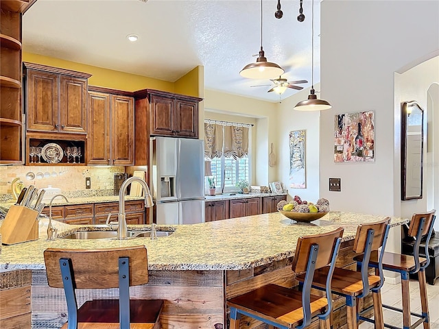 kitchen featuring arched walkways, open shelves, a sink, light stone countertops, and stainless steel fridge