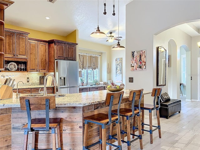 kitchen featuring tasteful backsplash, stainless steel fridge, a breakfast bar area, light stone counters, and open shelves