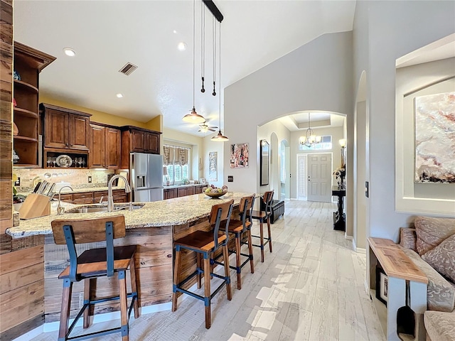 kitchen featuring arched walkways, visible vents, stainless steel refrigerator with ice dispenser, open shelves, and a sink