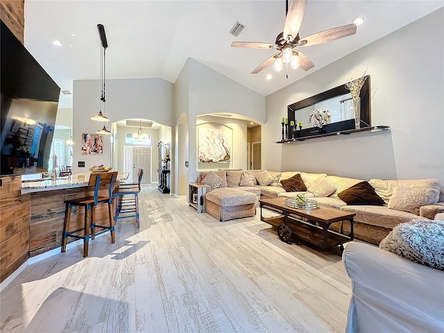 living room featuring arched walkways, visible vents, vaulted ceiling, ceiling fan, and light wood-type flooring