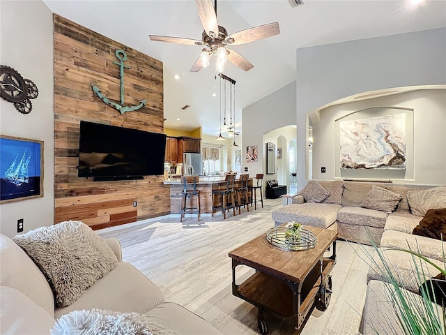 living area with arched walkways, ceiling fan, high vaulted ceiling, light wood-style flooring, and recessed lighting