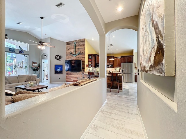 hall featuring arched walkways, light wood-type flooring, visible vents, and baseboards