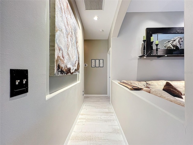 hallway with wood finished floors, visible vents, and baseboards