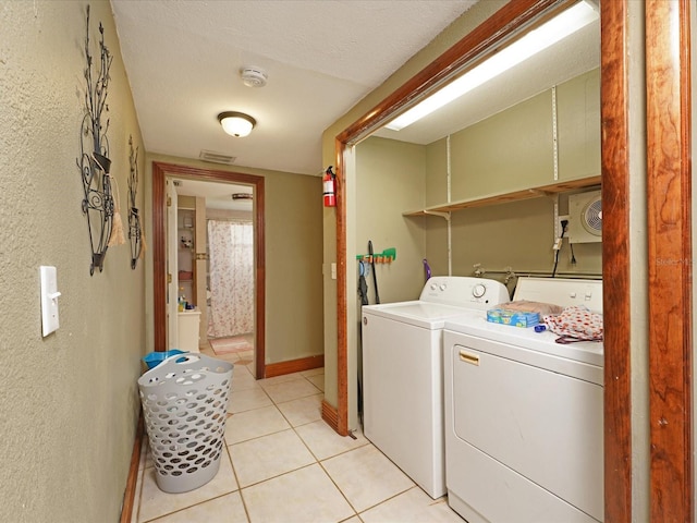 clothes washing area with independent washer and dryer, a textured ceiling, and light tile patterned floors