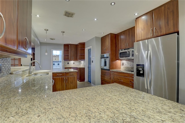 kitchen with pendant lighting, sink, light stone countertops, appliances with stainless steel finishes, and kitchen peninsula