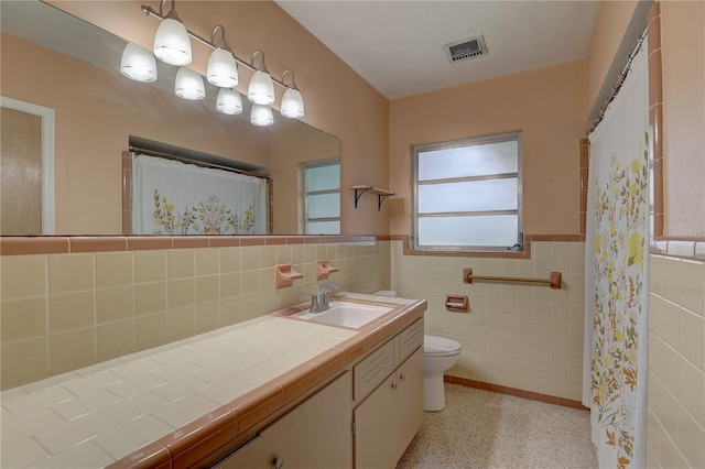 bathroom featuring vanity, toilet, and tile walls