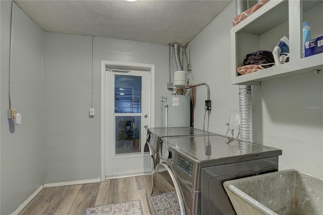 washroom with sink, washing machine and dryer, water heater, a textured ceiling, and hardwood / wood-style flooring