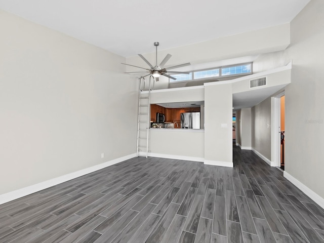 unfurnished living room featuring ceiling fan, dark hardwood / wood-style flooring, and a high ceiling