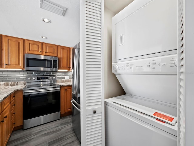 interior space with dark wood-type flooring, stacked washer and clothes dryer, decorative backsplash, light stone countertops, and stainless steel appliances