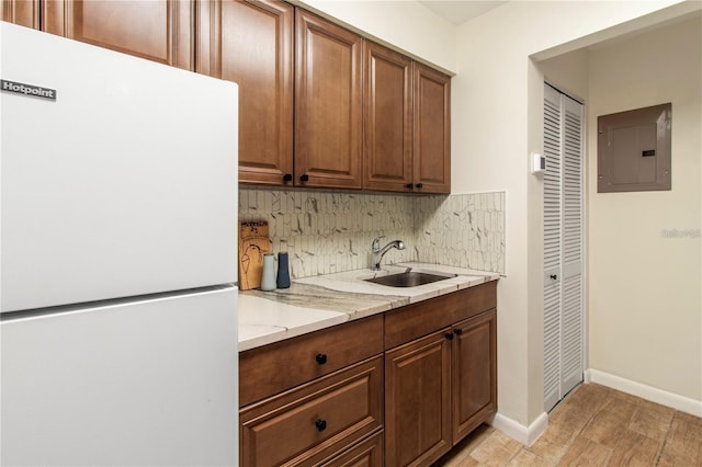 kitchen with light stone countertops, sink, backsplash, electric panel, and white fridge