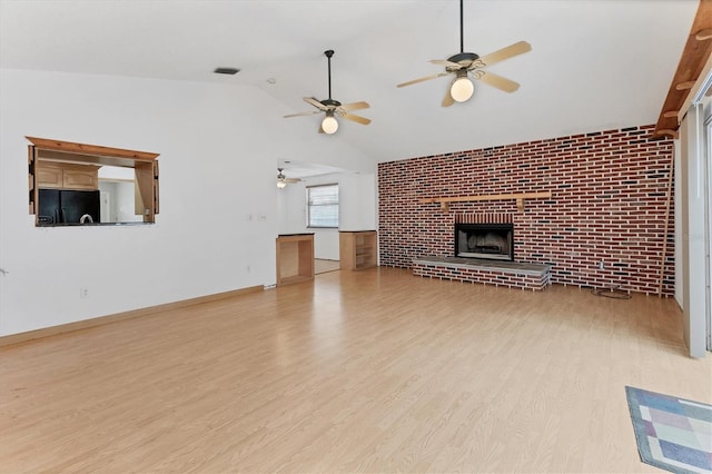 unfurnished living room featuring lofted ceiling, a brick fireplace, brick wall, and light hardwood / wood-style flooring