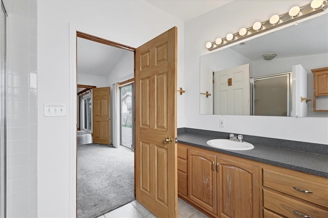 bathroom with a shower with shower door, vanity, vaulted ceiling, and tile patterned flooring