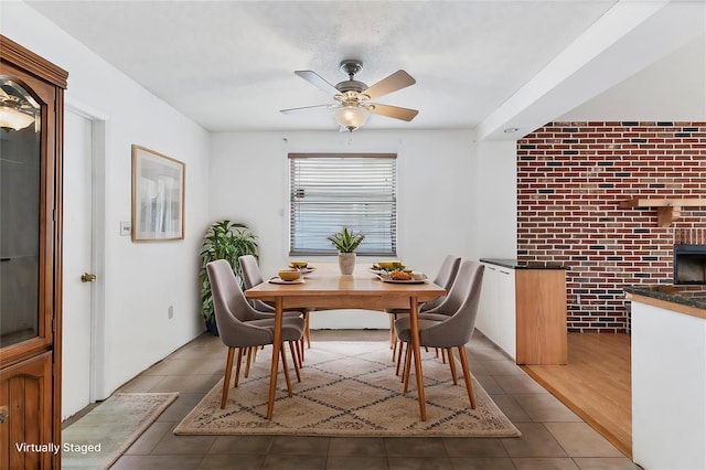 dining area featuring dark tile patterned floors, ceiling fan, and brick wall