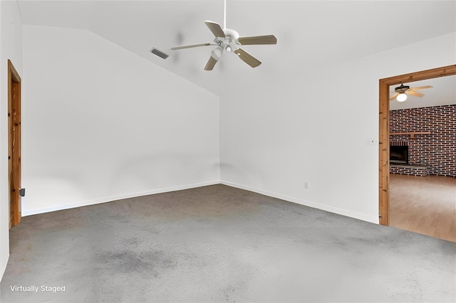 spare room with a brick fireplace, ceiling fan, and vaulted ceiling