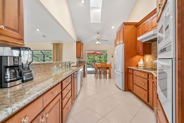 kitchen featuring white appliances, ceiling fan, lofted ceiling with skylight, a wealth of natural light, and backsplash