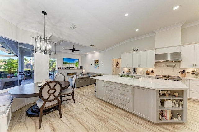 kitchen with a center island, light stone counters, range hood, pendant lighting, and ceiling fan with notable chandelier