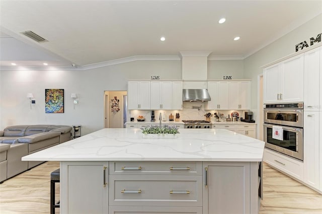 kitchen with light stone countertops, stainless steel appliances, a kitchen island, and exhaust hood