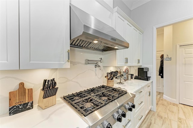 kitchen with white cabinetry, light stone countertops, wall chimney range hood, stainless steel gas cooktop, and tasteful backsplash